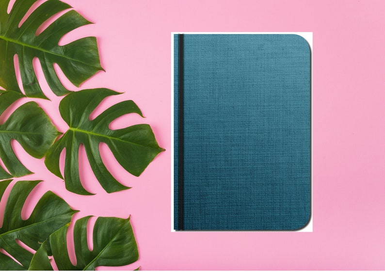 Puede incluir: Un cuaderno azul con una encuadernaci&oacute;n negra y una cubierta texturizada. El cuaderno est&aacute; sobre un fondo rosa con hojas verdes.