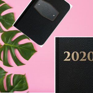 Puede incluir: Diario de cuero negro encuadernado con una inscripci&oacute;n dorada 2020. El diario est&aacute; rodeado de hojas verdes de monstera sobre un fondo rosa.