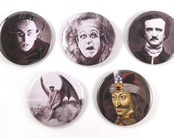May include: Five round button pins with black and white images of famous figures associated with vampires and horror. The images include a man with fangs, a man with a shocked expression, a man with a mustache, a winged demon, and a man with a crown.