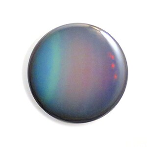 May include: A round, iridescent button with a blue, green, and purple gradient. The button has a slight sheen and three small red dots on the right side.