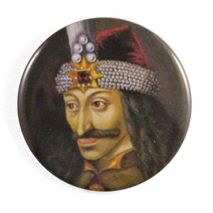 May include: A portrait of Vlad the Impaler, a historical figure, wearing a dark red and gold crown with a large ruby gemstone. He has a dark beard and mustache and is wearing a dark brown and gold tunic.