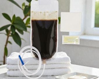 May include: A clear plastic enema bag filled with dark brown liquid, featuring an attached flexible white tube with a blue tip. Beside it are a square white pad and a small rectangular packet, with a bar of soap in a dish nearby.