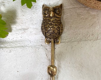 May include: A brass owl hook with a detailed design. The hook is attached to a round base and has a single hook.