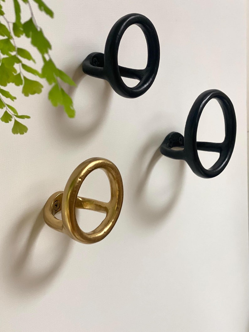 Puede incluir: Tres ganchos de pared decorativos, dos son negros y uno es dorado. Los ganchos tienen forma de c&iacute;rculo con un c&iacute;rculo m&aacute;s peque&ntilde;o cortado en el centro.
