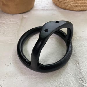 Puede incluir: Colgador de plantas de metal negro con un dise&ntilde;o curvo y tres agujeros.