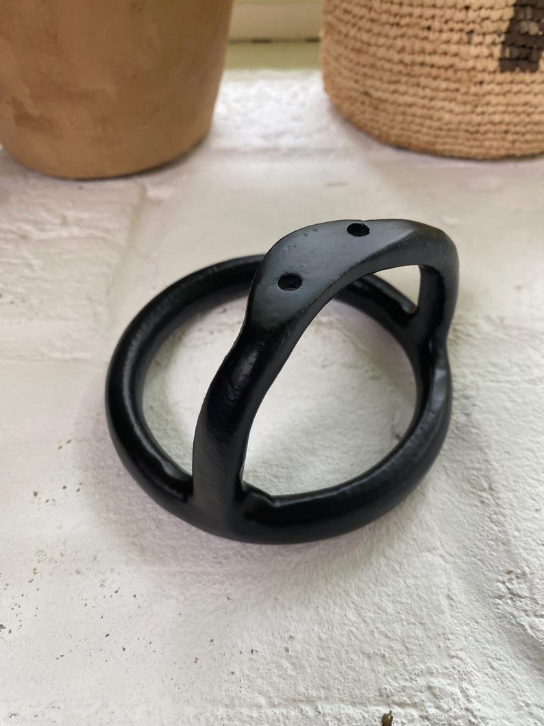 Puede incluir: Colgador de plantas de metal negro con un dise&ntilde;o curvo y tres agujeros.