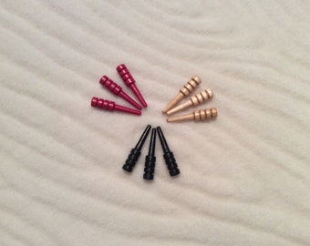 May include: Nine wooden game pieces in three colors: red, black, and natural wood. The pieces are arranged in a circle on a white surface.