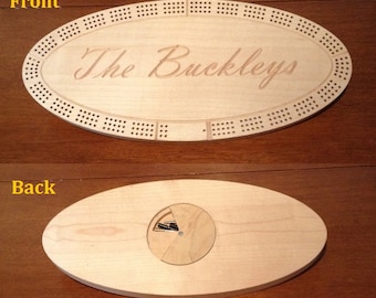 May include: A wooden cribbage board with the inscription "The Buckleys" on the front. The back of the board has a circular compartment for storing the pegs.