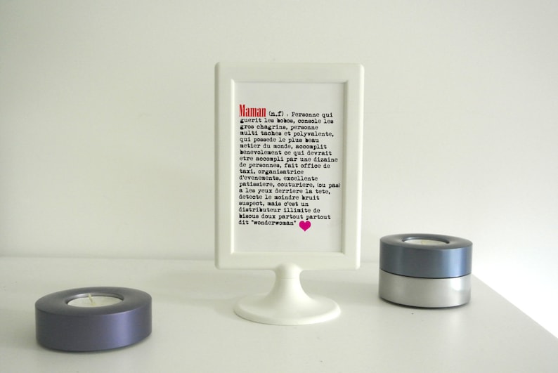 May include: A white picture frame with a black and white text description of the word 'Maman' in French. The text reads: 'Maman (n.f.) Personne qui guerit les bobos, console les gros chagrins, personne multi taches et polyvalente, qui possede le plus beau metier du monde, accomplit benevolement ce qui devrait etre accompli par une dizaine de personnes, fait office de taxi, organisatrice d'evenements, excellente patissiere, couturiere, tou pas a les yeux derriere la tete, detecte le moindre bruit suspect, mais c'est un distributeur illimite de bisous doux partout partout dit 'wonderwoman''