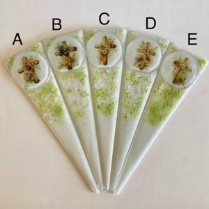 May include: Five decorative glass pieces, each with a unique design. Each piece has a white base with green speckles and a circular image of a cross adorned with flowers. The pieces are arranged in a fan shape.