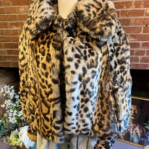 K&ouml;nnte beinhalten: Eine kurz geschnittene Jacke mit einem auff&auml;lligen Leopardenmuster in Braun-, Beige- und Schwarzt&ouml;nen. Das Kleidungsst&uuml;ck hat einen gro&szlig;en, abgerundeten Kragen, lange &Auml;rmel mit eng anliegenden B&uuml;ndchen und einen Knebelverschluss am Ausschnitt.