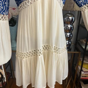 Pu&ograve; includere: Un vestito color crema con maniche e corpetto ricamati in blu. L'abito presenta un design all'uncinetto sullo scollo e in vita, e una gonna fluida. Le maniche sono lunghe e ampie, e l'abito &egrave; realizzato in un tessuto leggero.