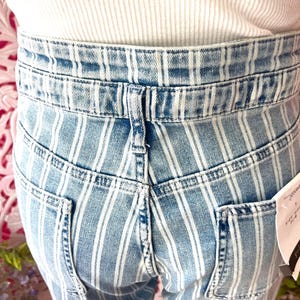 Pode incluir: Cal&ccedil;as de ganga azul claro com riscas brancas verticais. As cal&ccedil;as de ganga t&ecirc;m dois bolsos traseiros e uma cintura com presilhas. A pessoa est&aacute; a usar um top branco canelado.