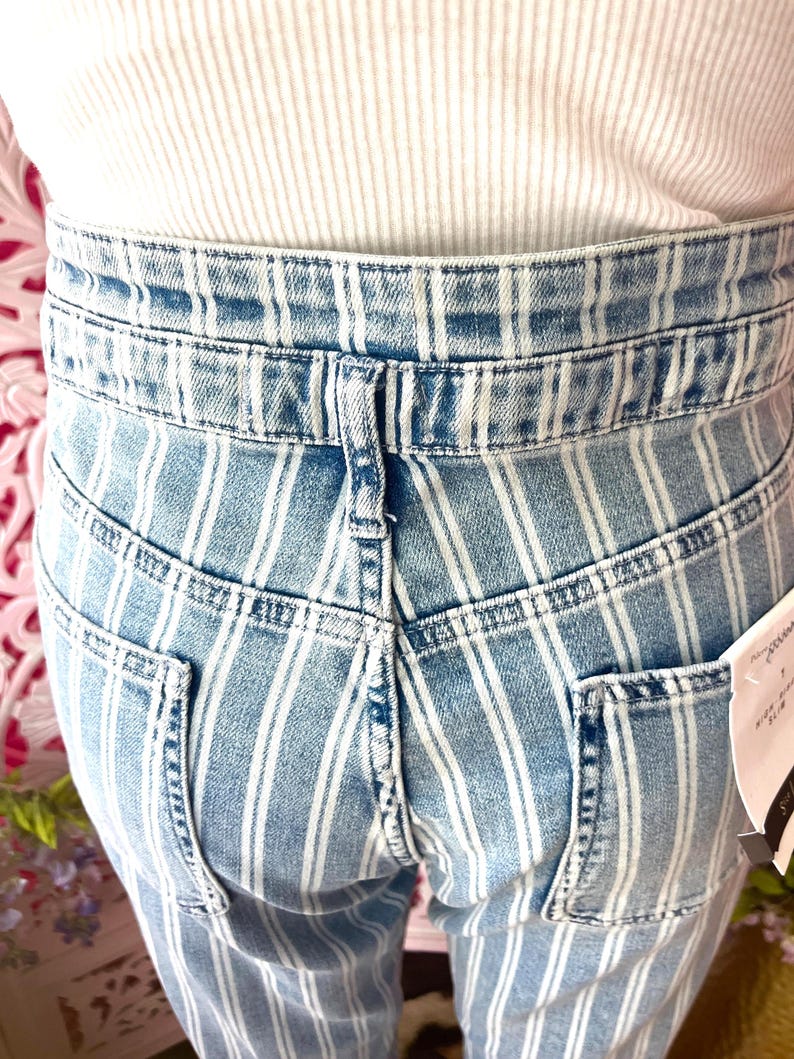 Pode incluir: Cal&ccedil;as de ganga azul claro com riscas brancas verticais. As cal&ccedil;as de ganga t&ecirc;m dois bolsos traseiros e uma cintura com presilhas. A pessoa est&aacute; a usar um top branco canelado.