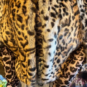 K&ouml;nnte beinhalten: Eine kurze Kunstfelljacke mit einem braunen, schwarzen und beigen Leopardenmuster. Die Jacke wird &uuml;ber einem lang&auml;rmeligen Oberteil mit passendem Leopardenmuster und einer hellblauen, s&auml;uregewaschenen Jeans mit sichtbarem Knopf getragen.