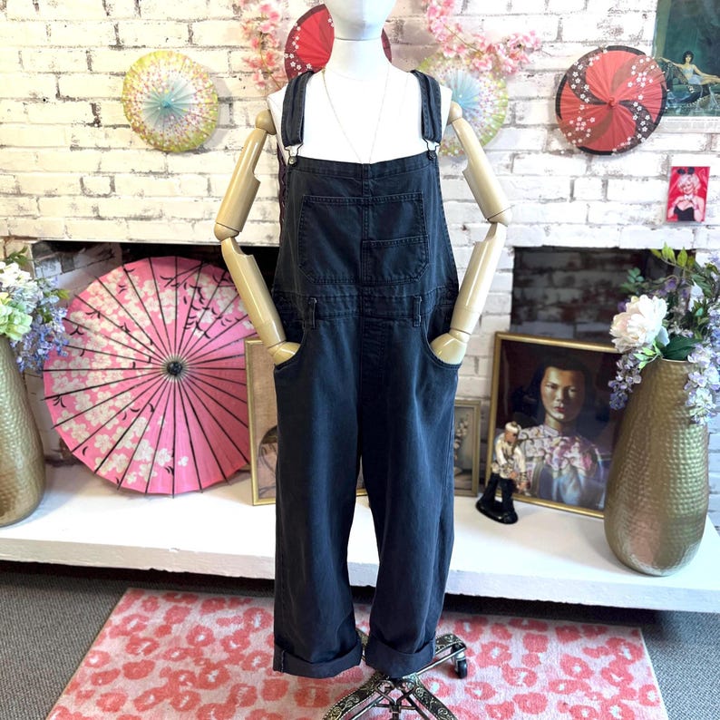 May include: Dark gray denim overalls with adjustable straps, front pockets, and rolled cuffs. The overalls are displayed on a mannequin. The overall style is casual and relaxed.