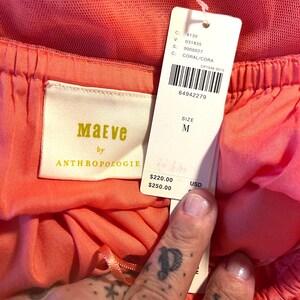 Puede incluir: Primer plano de una prenda de color coral con una etiqueta. La etiqueta dice "Maeve by Anthropologie" e incluye la talla "M". La prenda tiene un dise&ntilde;o en capas con una superposici&oacute;n de tul. El color es "CORAL/CORA".