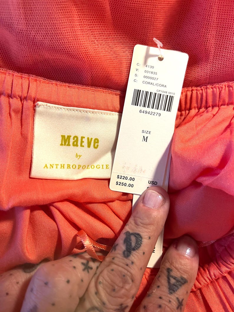 Puede incluir: Primer plano de una prenda de color coral con una etiqueta. La etiqueta dice "Maeve by Anthropologie" e incluye la talla "M". La prenda tiene un dise&ntilde;o en capas con una superposici&oacute;n de tul. El color es "CORAL/CORA".