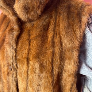 May include: A brown fur coat with a large collar. The coat has a button closure and a soft, textured appearance. The fur is a rich, warm brown color.
