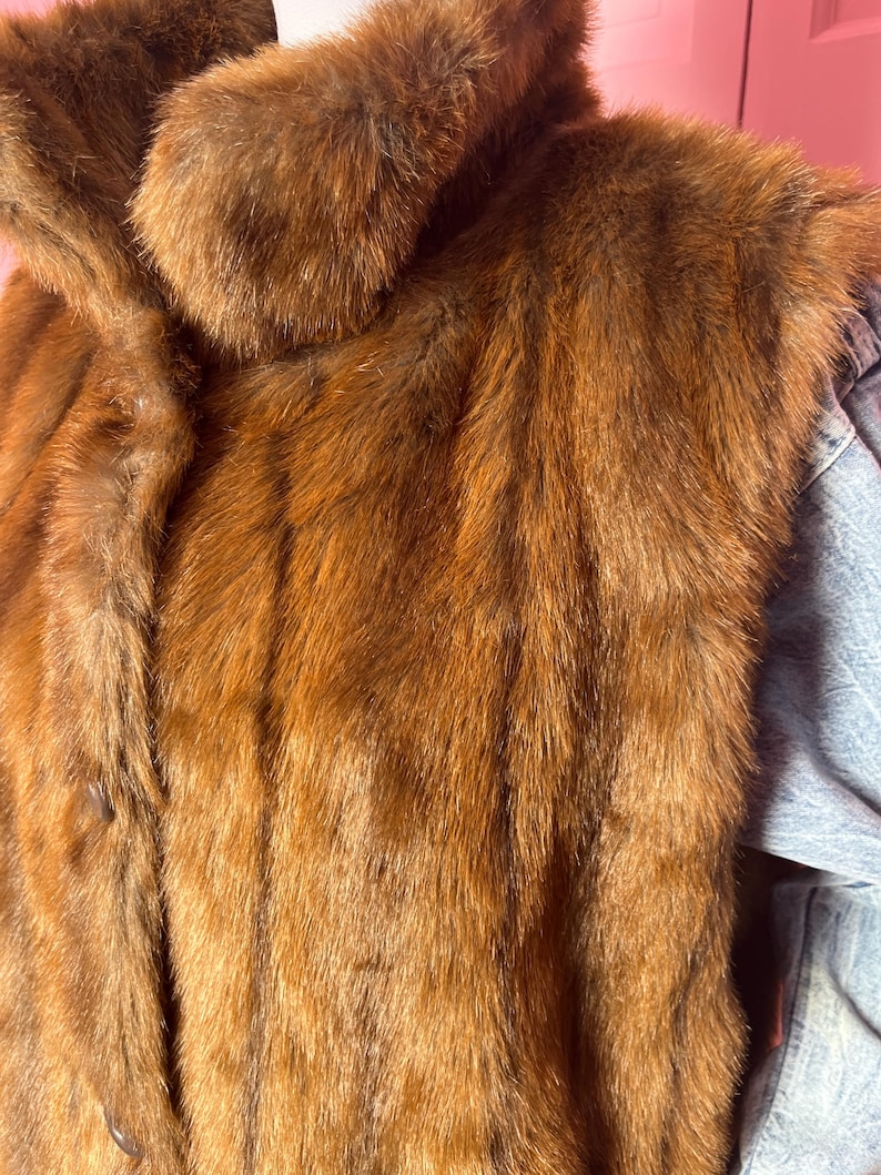 May include: A brown fur coat with a large collar. The coat has a button closure and a soft, textured appearance. The fur is a rich, warm brown color.