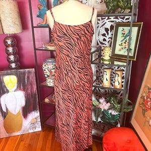 Puede incluir: Vestido lencero color coral con estampado de cebra negro. El vestido tiene tirantes finos y largo midi. Se exhibe en un maniqu&iacute; frente a una estanter&iacute;a de metal negro con objetos decorativos.