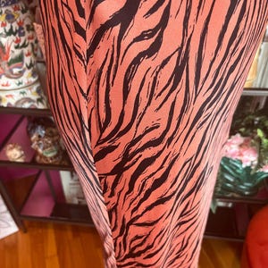 Puede incluir: Primer plano de un vestido color coral con un estampado de rayas de cebra negras. La tela parece ser un material ligero. El vestido tiene una costura vertical en la parte delantera.