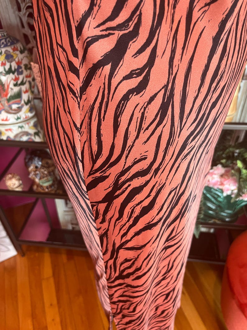 Puede incluir: Primer plano de un vestido color coral con un estampado de rayas de cebra negras. La tela parece ser un material ligero. El vestido tiene una costura vertical en la parte delantera.