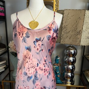 May include: A light purple slip dress with a floral pattern in shades of pink, blue, and purple. The dress has thin straps and is displayed on a mannequin. A gold leaf pendant hangs from a delicate chain.
