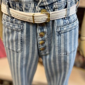 Pode incluir: Jeans azuis e brancos listrados com cintura alta e braguilha de bot&otilde;es. Os jeans t&ecirc;m um cinto creme com fivela dourada. Os bolsos s&atilde;o vis&iacute;veis e o tecido tem um aspeto ligeiramente desbotado.