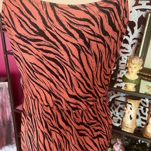 Puede incluir: Vestido lencero color coral con estampado de rayas de cebra negras. El vestido presenta finas tiras de espagueti y un dise&ntilde;o sencillo y elegante. La tela parece ligera y fluida, adecuada para climas c&aacute;lidos.