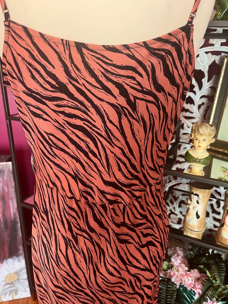 Puede incluir: Vestido lencero color coral con estampado de rayas de cebra negras. El vestido presenta finas tiras de espagueti y un dise&ntilde;o sencillo y elegante. La tela parece ligera y fluida, adecuada para climas c&aacute;lidos.