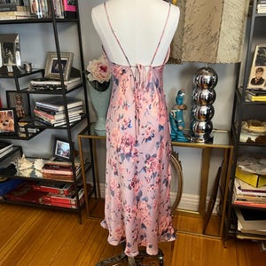 May include: A light pink floral print slip dress on a mannequin. The dress features a delicate floral pattern in shades of pink and blue. The dress has spaghetti straps and a flowing silhouette, perfect for a special occasion.
