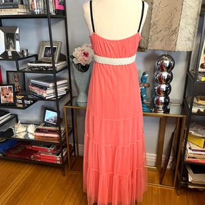 Puede incluir: Vestido largo color coral con cintur&oacute;n de cuerda blanco y tirantes finos negros. El vestido se exhibe en un maniqu&iacute;. El vestido tiene una falda escalonada y est&aacute; hecho de una tela transparente.