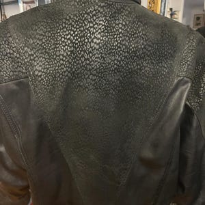 May include: Black leather jacket with a high collar. The upper back and shoulders feature a textured, leopard-print design. The jacket has a V-shaped panel on the back and a classic, tailored fit.