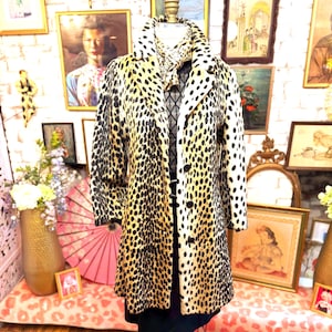 May include: A long-sleeved coat featuring a tan and black leopard print pattern, a notched collar, and a front button closure. The coat is displayed on a mannequin and includes a matching leopard print scarf tied around the neck area.
