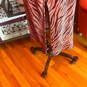 Puede incluir: Un vestido largo con un vibrante fondo coral y audaces rayas de cebra negras. El vestido se exhibe en un maniqu&iacute; de metal negro con ruedas, mostrando su dise&ntilde;o y silueta. El vestido tiene una abertura frontal.