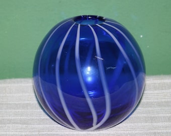May include: A cobalt blue glass vase with white stripes. The vase is round and has a wide opening.