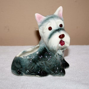 Può includere: Un vaso da fiori in ceramica a forma di cane terrier bianco e nero seduto con orecchie rosa e occhi rossi. Il cane ha la faccia bianca e il corpo nero. Il vaso ha un foro nella parte superiore per piantare.