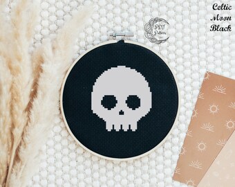 May include: A black and white cross-stitch pattern of a skull on black fabric in a round embroidery hoop. The text "Celtic Moon Black" is visible in the upper right corner of the image.