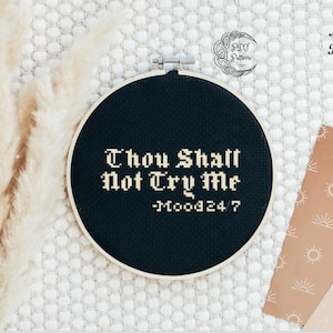 Op de afbeelding: Zwarte borduurring met witte kruissteektekst die "Thou Shall Not Try Me -Mood 24/7" luidt.