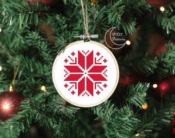 Puede incluir: Patrón de punto de cruz rojo y blanco de un adorno de copo de nieve colgado de un árbol de Navidad. El adorno está en un aro de bordado redondo.