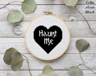 May include: Black and white cross-stitch embroidery hoop with a black heart that says "Haunt Me" in white text.