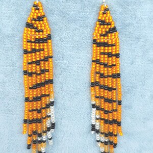May include: A pair of long, beaded earrings with a tiger stripe pattern in orange, black, and white.