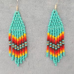 May include: A pair of turquoise and orange beaded earrings with silver hooks. The earrings are made with small seed beads and feature a geometric pattern.