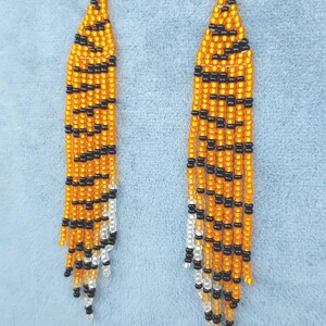 May include: A pair of long, beaded earrings with a tiger stripe pattern in orange, black, and white.