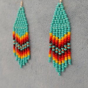 May include: A pair of turquoise, red, orange and yellow beaded earrings. The earrings are long and dangle, with a silver hook.