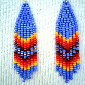 May include: A pair of long, beaded earrings with a blue, orange, red and brown colour scheme. The earrings are teardrop shaped and have a fringe at the bottom.