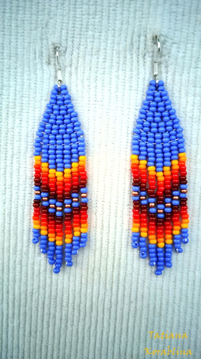 May include: A pair of long, beaded earrings with a blue, orange, red and brown colour scheme. The earrings are teardrop shaped and have a fringe at the bottom.