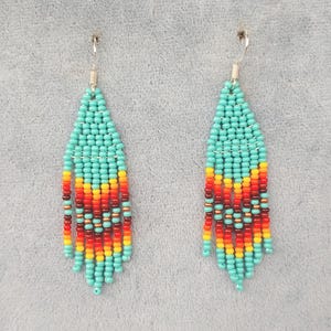 May include: A pair of turquoise, red, orange and yellow beaded dangle earrings. The earrings are made with small seed beads and have a fringe-like design.