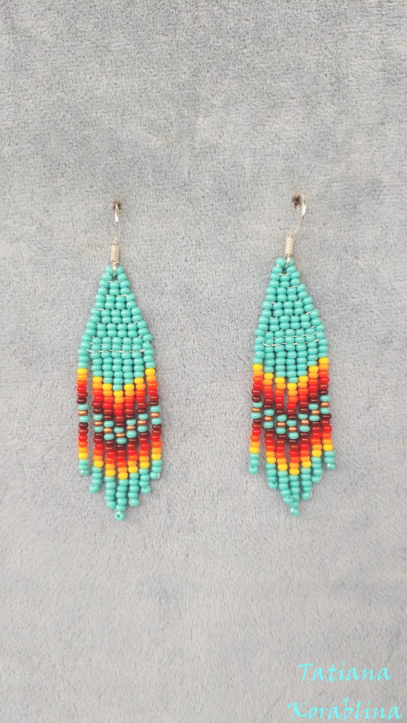 May include: A pair of turquoise, red, orange and yellow beaded dangle earrings. The earrings are made with small seed beads and have a fringe-like design.